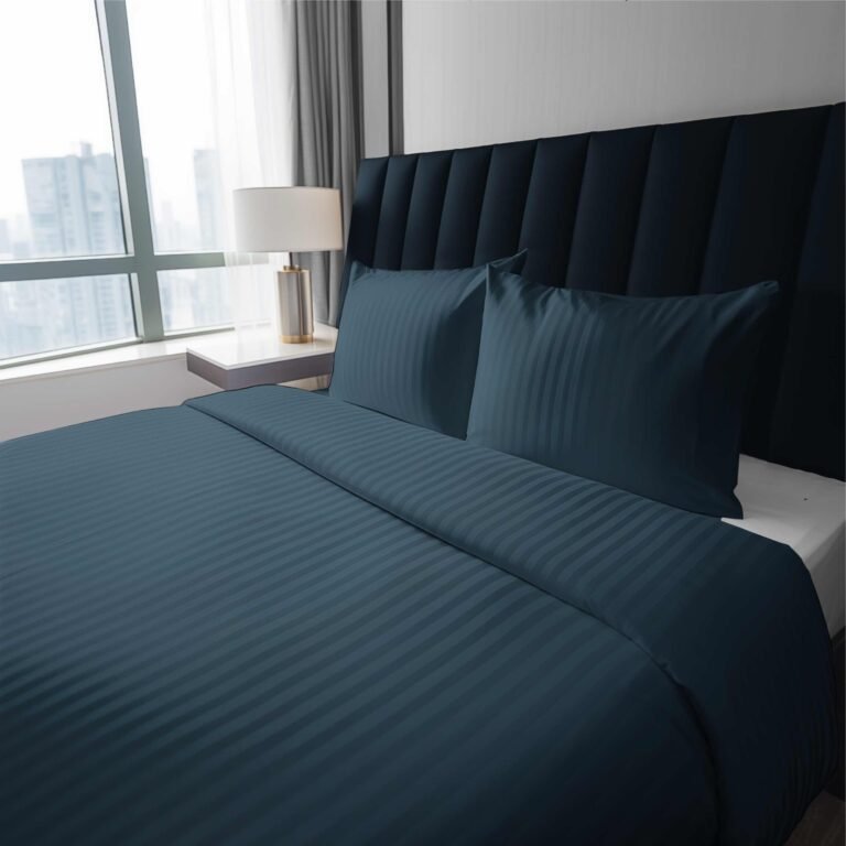 Zdjęcie przedstawiające komplet pościeli w kolorze ciemnoniebieskim wykonany z luksusowej bawełny adamaszkowej. Delikatny połysk i subtelne prążki nadają tkaninie elegancki charakter. Pościel zaprezentowana w nowoczesnej sypialni z dużym oknem i tapicerowanym zagłówkiem.