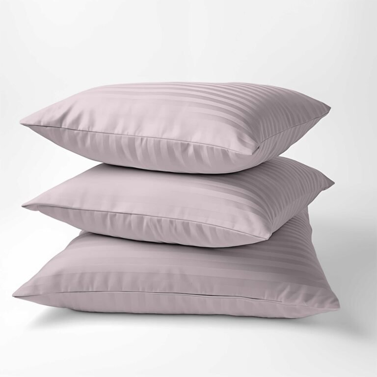 Zdjęcie przedstawiające Trzy poduszki w poszewkach z adamaszku w kolorze pudrowego różu, ułożone jedna na drugiej. Tkanina wykonana z luksusowej 100% bawełny o delikatnym połysku i subtelnym wzorze w paski, zaprezentowana na białym tle.