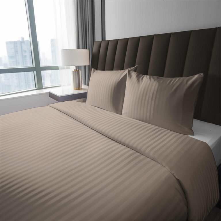 Zdjęcie przedstawiające Komplet pościeli z adamaszku w kolorze taupe ułożony na łóżku w eleganckiej sypialni hotelowej z dużym oknem i widokiem na miasto; nowoczesne wnętrze z tapicerowanym zagłówkiem i lampą nocną.