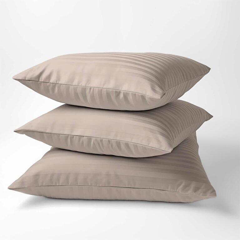 Zdjęcie przedstawiające Trzy beżowe poduszki w poszewkach z adamaszku w kolorze taupe, ułożone jedna na drugiej na białym tle.